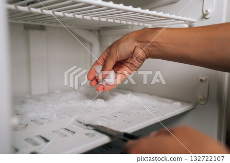 Cropped shot of man using knife to remove ice buildup from inside refrigerator, highlighting concept of defrosting and kitchen maintenance. Concept of domestic work, housekeeping and household. Cropped shot of man using knife to remove ice buildup from inside refrigerator, highlighting concept of defrosting and kitchen maintenance. Concept of domestic work, housekeeping and household. 132722107