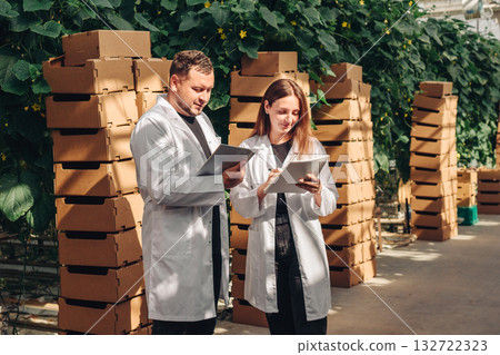 Scientists examining cartons, Scientists in coats assess stacked packaging beside plant nursery, Group of researchers inspecting and recording data on cardboard packages near garden center Scientists examining cartons, Scientists in coats assess stacked packaging beside plant nursery, Group of researchers inspecting and recording data on cardboard packages near garden center 132722323