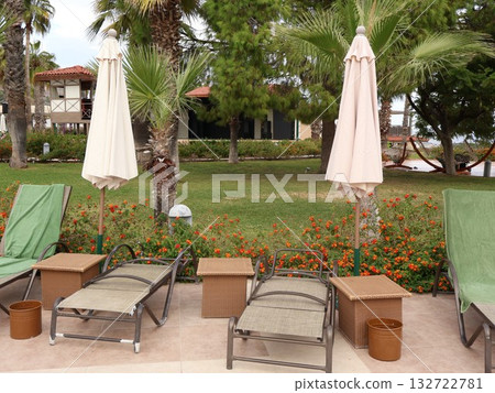 Relaxing Poolside Lounge Area With Umbrellas, Palm Trees, And Floral Garden At Resort Relaxing Poolside Lounge Area With Umbrellas, Palm Trees, And Floral Garden At Resort 132722781