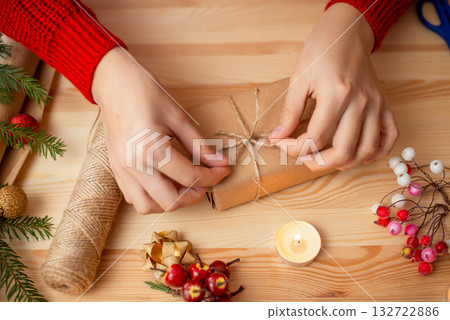 Top view of woman hands making bow on little gift box. Christmas and New Year time, preparing presents and decoration for holidays Top view of woman hands making bow on little gift box. Christmas and New Year time, preparing presents and decoration for holidays 132722886