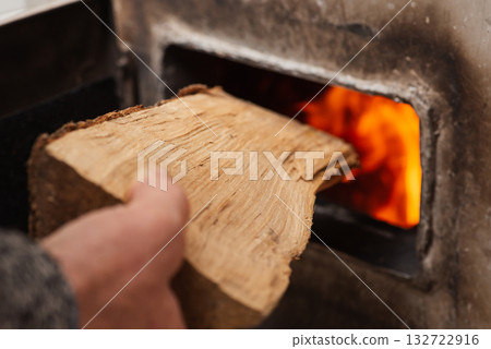 Man loads piece of firewood in the solid fuel boiler, flames on the background. Solid fuel and heating concept 132722916