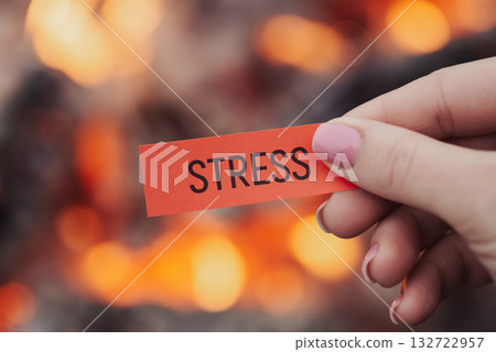 Female hand holding red small sheet of paper with word "stress", bonfire on background, close up. Concept of relaxation, releasing of stress, tension and anxiety 132722957