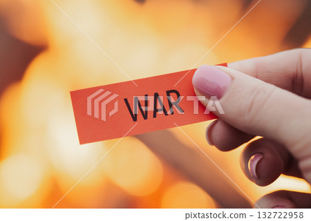 Small red sheet of paper in hand of a girl with word "war" on it, close up, fire on the background. Conflict, combat, fighting, military actions, desire to stop and end all this nightmare 132722958