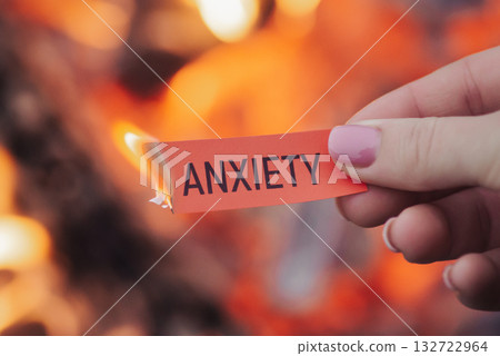 Small burning red sheet of paper with word Anxiety on it in female hand, close up. Concept of releasing of fear, pain, problems and worry 132722964
