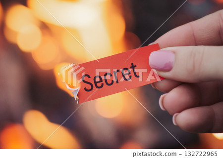 Female hand holding small red burning sheet of paper with word "secret" on it , close up. Concept of opening the truth, being sincere and honest 132722965