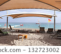 Sunny Beachfront Lounge Chairs Under Shade Canopies Over Pebble Beach by Calm Sea 132723002