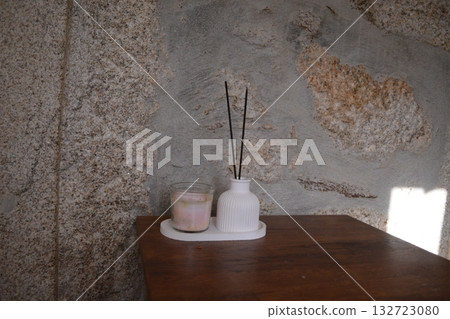 Minimalist bedroom decor with a wooden nightstand and items on it - a flower pot, incense sticks, flowers, and a vase. A homey, detailed concept. Minimalist bedroom decor with a wooden nightstand and items on it - a flower pot, incense sticks, flowers, and a vase. A homey, detailed concept. 132723080