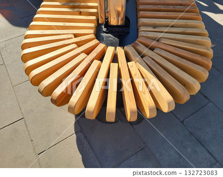 A semi-circular wooden light brown curved bench in a park on a bright sunny day. A semi-circular wooden light brown curved bench in a park on a bright sunny day. 132723083