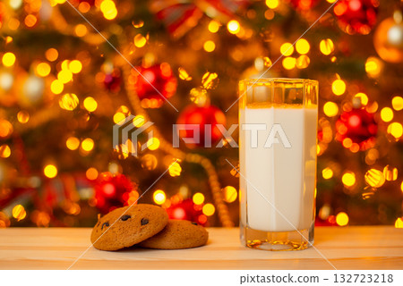 Glass of milk and some cookies on table on background of Christmas lights. Milk and snack for Santa concept Glass of milk and some cookies on table on background of Christmas lights. Milk and snack for Santa concept 132723218