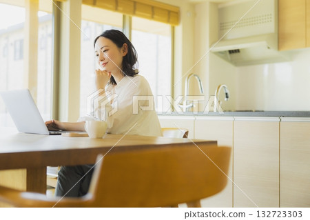 使用個人計算機的婦女在廚房裡 使用個人計算機的婦女在廚房裡 132723303