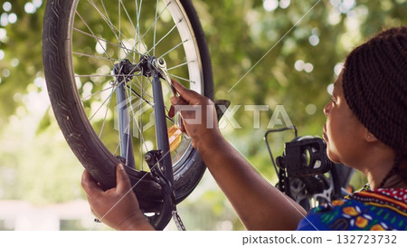 Sporty african american female cyclist uses spanner for tightening bicycle tire safely for outside cycling. Black woman performing bike maintenance with wrench as specialized work tool. 132723732