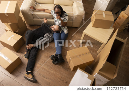 Multiethnic couple rests on floor surrounded by cardboard boxes during moving day. Caucasian boyfriend and black girlfriend bond while starting new chapter in cozy apartment after relocation. 132723734