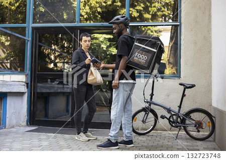 African American courier holds a portable POS terminal as the customer pays with a contactless payment. modern meal order exchange reflects quick service and mobile banking purchase. 132723748