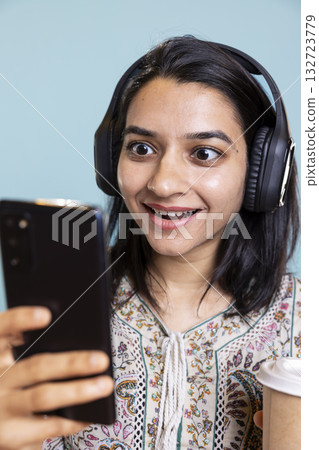 Excited jolly indian girl selecting music from her smartphone and serves coffee, enjoying free time with leisure activity in the studio. Happy relaxed woman dancing on groovy songs. Excited jolly indian girl selecting music from her smartphone and serves coffee, enjoying free time with leisure activity in the studio. Happy relaxed woman dancing on groovy songs. 132723779