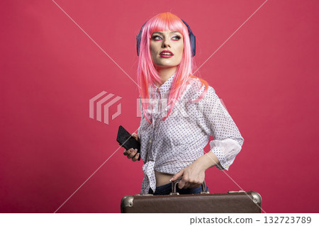 Young traveler with suitcase and mobile device, listening to music and navigating the terminal. Caucasian lady in casual outfit holding luggage and smartphone, enjoying tunes through wireless headset. 132723789