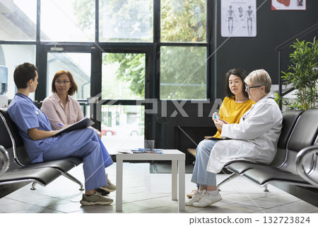 General practitioner preparing glucose test strip for sugar level monitoring in waiting room facility. Asian patient receives guidance on hyperglycemia warning signs and glucose control methods. 132723824