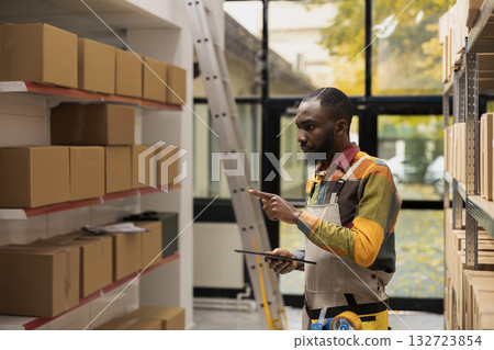 Small business worker checking inventory and preparing parcels for delivery, using a tablet to ensure quality control for shipment services. E-commerce operations and product handling. 132723854