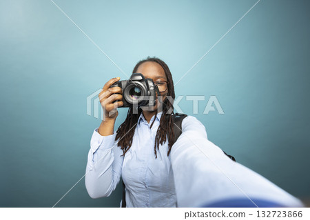Black female photographer records herself, smiling toward device while holding DSLR close to her face. Pov of african american woman taking selfie and using digital camera, showing photography skills. 132723866