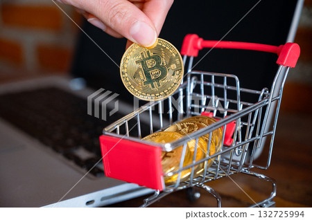 Someone hand try to put a Bitcoin token in a trolley toy on laptop. Bitcoin is one of the popular cryptocurrency, a virtual currency or a digital currency. 132725994