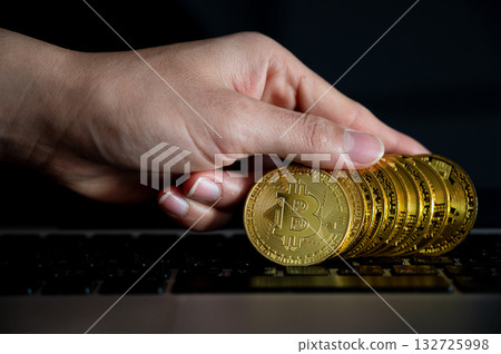 Close up of human hand holding some pieces of golden Bitcoin token on laptop. Bitcoin is one of the popular cryptocurrency, a virtual currency or a digital currency. Close up of human hand holding some pieces of golden Bitcoin token on laptop. Bitcoin is one of the popular cryptocurrency, a virtual currency or a digital currency. 132725998