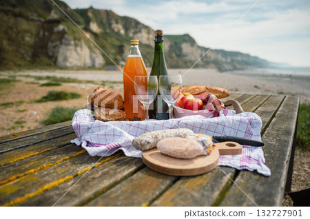 A cozy beach picnic in Normandy featuring French cidre, regional cheese, and fresh apples, set against a scenic coastal backdrop A cozy beach picnic in Normandy featuring French cidre, regional cheese, and fresh apples, set against a scenic coastal backdrop 132727901