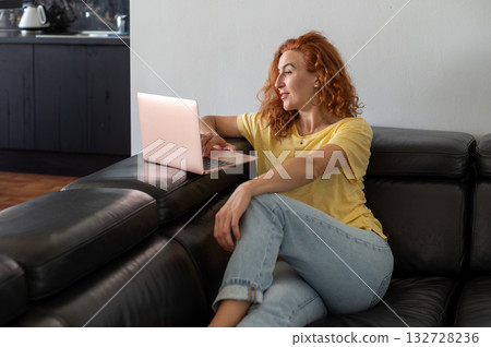 Young woman focused on her laptop while working remotely from the comfort of her home workspace. 132728236