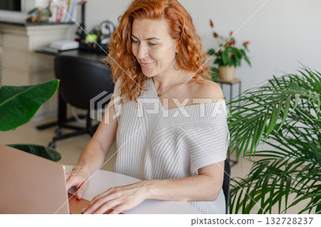 Young woman focused on her laptop while working remotely from the comfort of her home workspace. Young woman focused on her laptop while working remotely from the comfort of her home workspace. 132728237