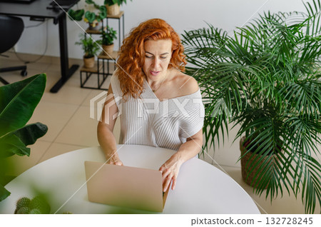 Young woman focused on her laptop while working remotely from the comfort of her home workspace. Young woman focused on her laptop while working remotely from the comfort of her home workspace. 132728245