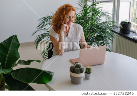 Young woman focused on her laptop while working remotely from the comfort of her home workspace. Young woman focused on her laptop while working remotely from the comfort of her home workspace. 132728246