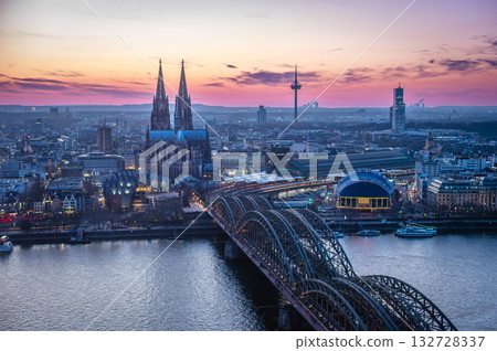 A breathtaking view of the Cologne skyline right after sunset featuring the iconic Cologne Cathedral and the city's famous bridge. The warm hues of the evening sky create a stunning scene in Germany. 132728337