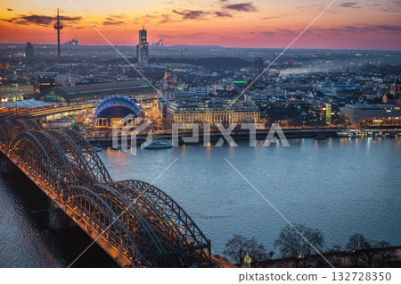 A breathtaking view of the Cologne skyline right after sunset featuring the iconic Cologne Cathedral and the city's famous bridge. The warm hues of the evening sky create a stunning scene in Germany. A breathtaking view of the Cologne skyline right after sunset featuring the iconic Cologne Cathedral and the city's famous bridge. The warm hues of the evening sky create a stunning scene in Germany. 132728350