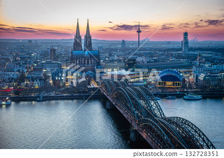 A breathtaking view of the Cologne skyline right after sunset featuring the iconic Cologne Cathedral and the city's famous bridge. The warm hues of the evening sky create a stunning scene in Germany. 132728351