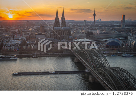 A breathtaking view of the Cologne skyline during sunset featuring the iconic Cologne Cathedral and the city's famous bridge. The warm hues of the evening sky create a stunning scene in Germany. A breathtaking view of the Cologne skyline during sunset featuring the iconic Cologne Cathedral and the city's famous bridge. The warm hues of the evening sky create a stunning scene in Germany. 132728376