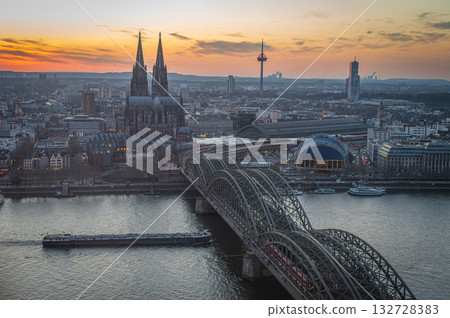 A breathtaking view of the Cologne skyline during sunset featuring the iconic Cologne Cathedral and the city's famous bridge. The warm hues of the evening sky create a stunning scene in Germany. A breathtaking view of the Cologne skyline during sunset featuring the iconic Cologne Cathedral and the city's famous bridge. The warm hues of the evening sky create a stunning scene in Germany. 132728383