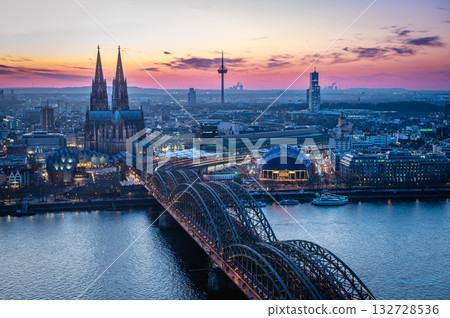 A breathtaking view of the Cologne skyline right after sunset featuring the iconic Cologne Cathedral and the city's famous bridge. The warm hues of the evening sky create a stunning scene in Germany. 132728536