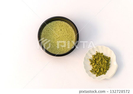 A vibrant green matcha drink alongside a bowl of fine matcha powder, presented on a clean white background for a fresh and minimalistic look. 132728572