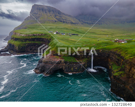 Dramatic Mulafossur waterfall plunging into the ocean with Gasadalur village and cliffs in the background. 132728640