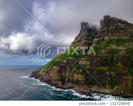 Dramatic Mulafossur waterfall plunging into the ocean with Gasadalur village and cliffs in the background. 132728648