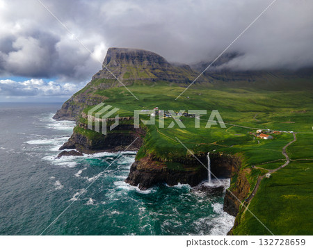 Dramatic Mulafossur waterfall plunging into the ocean with Gasadalur village and cliffs in the background. Dramatic Mulafossur waterfall plunging into the ocean with Gasadalur village and cliffs in the background. 132728659