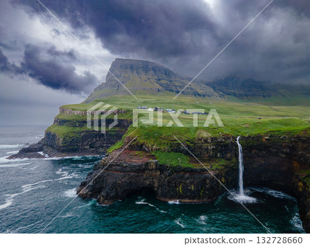Dramatic Mulafossur waterfall plunging into the ocean with Gasadalur village and cliffs in the background. Dramatic Mulafossur waterfall plunging into the ocean with Gasadalur village and cliffs in the background. 132728660