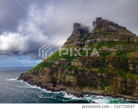 Dramatic Mulafossur waterfall plunging into the ocean with Gasadalur village and cliffs in the background. Dramatic Mulafossur waterfall plunging into the ocean with Gasadalur village and cliffs in the background. 132728697