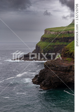 Dramatic Mulafossur waterfall plunging into the ocean with Gasadalur village and cliffs in the background. Dramatic Mulafossur waterfall plunging into the ocean with Gasadalur village and cliffs in the background. 132728706