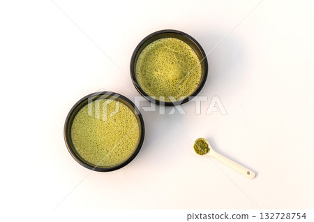 A vibrant green matcha drink alongside a bowl of fine matcha powder, presented on a clean white background for a fresh and minimalistic look. A vibrant green matcha drink alongside a bowl of fine matcha powder, presented on a clean white background for a fresh and minimalistic look. 132728754