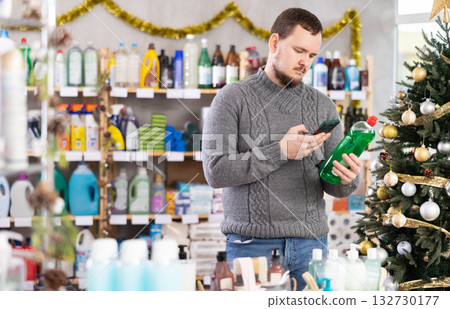 Young shopper scanning bottle of dishwashing liquid in festively decorated store 132730177