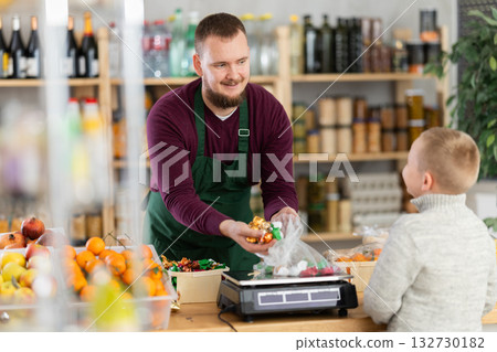 Friendly seller weighing and selling candies to little customer in grocery store Friendly seller weighing and selling candies to little customer in grocery store 132730182