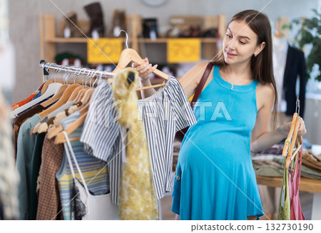 Young expecting woman choosing summer dresses in outlet store Young expecting woman choosing summer dresses in outlet store 132730190