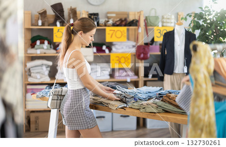 Young woman customer making choice and elect trousers or shorts in store 132730261