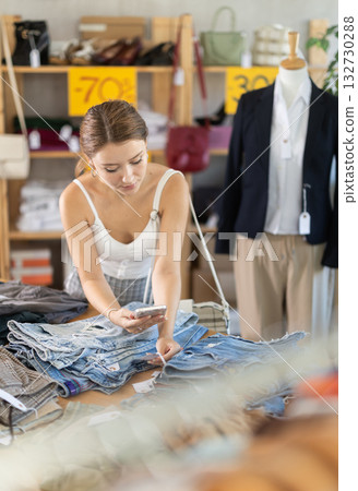 While shopping, girl scans barcode on label of denim trousers or shorts, 132730288