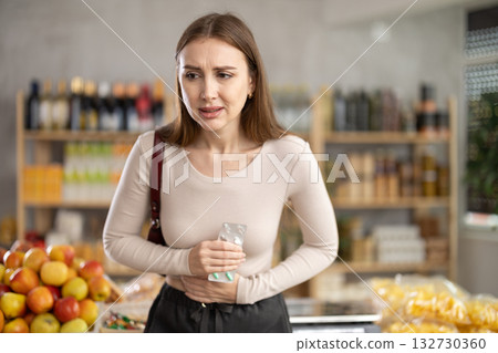 Young woman with stomach pain pills in grocery store Young woman with stomach pain pills in grocery store 132730360