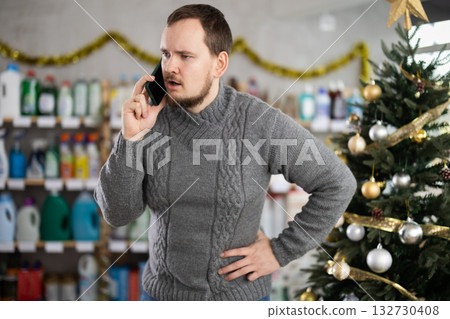Middle-aged guy speaking on mobile phone while shopping in store during Christmas Middle-aged guy speaking on mobile phone while shopping in store during Christmas 132730408